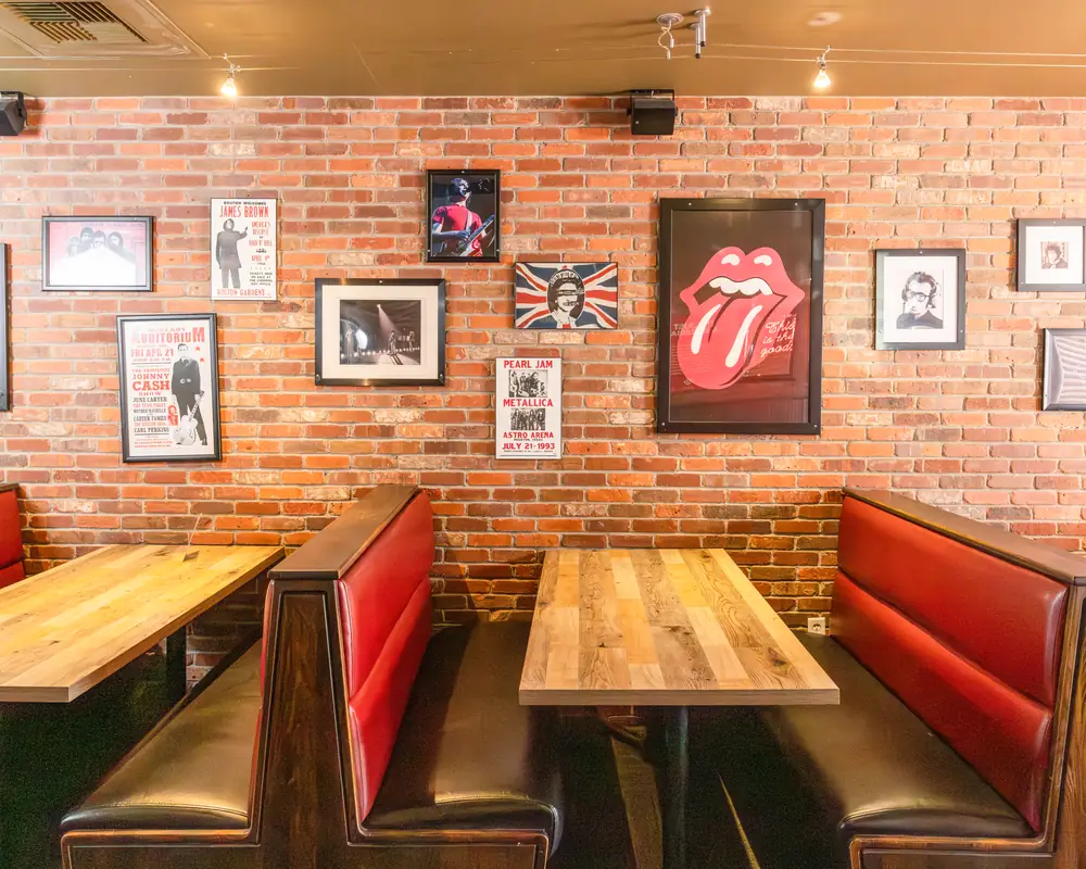 Brick wall with framed rock posters above red booths at Durkin&rsquo;s Pizza in McKinney, TX